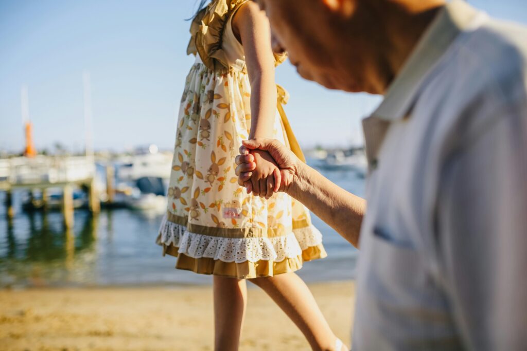 pexels-photo-5637741-5637741 A touching scene of a grandfather holding his granddaughter's hand by the seaside on a sunny day.